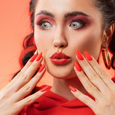 Mulher com maquilhagem vermelha e unhas vermelhas brilhantes em fundo laranja