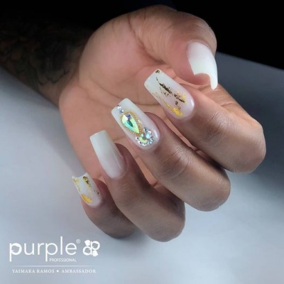 Unhas artificiais decoradas com brilhos dourados e pedras brilhantes em tons brancos e translúcidos