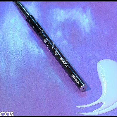 Caneta de precisão preta INOCOS para unhas com mancha cremosa branca em fundo violeta