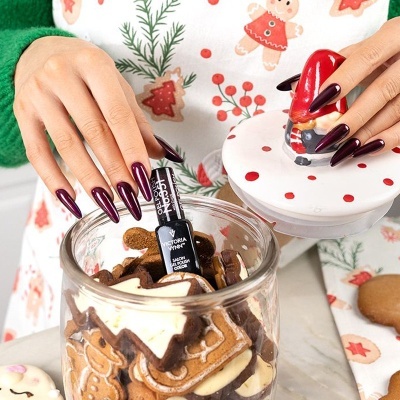 Frascos de verniz de gel preto Victoria Vynn com biscoitos decorativos e mãos com unhas vermelhas compridas