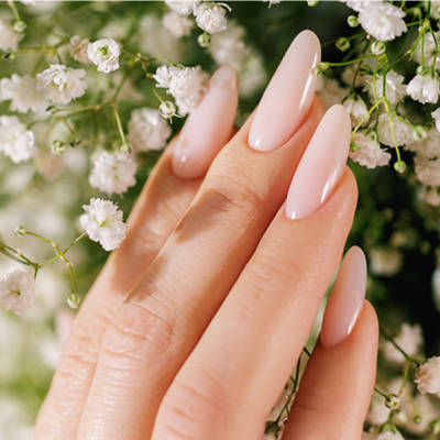 Mão com unhas nude brilhosas e flores brancas delicadas ao fundo