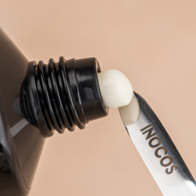 Tubo preto com creme branco a sair e espátula metálica INOCOS