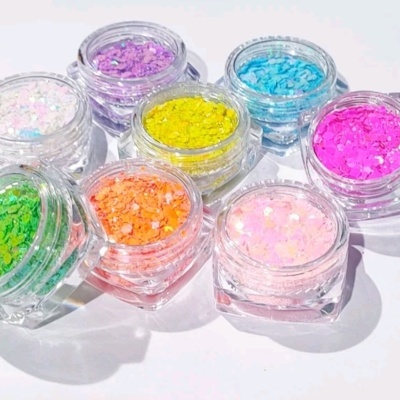 Sete frascos pequenos com glitter colorido variados sobre superfície branca