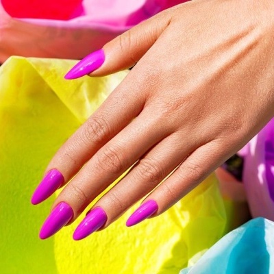 Mão feminina com unhas rosa vibrantes sobre papéis coloridos.