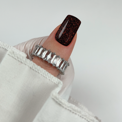 Anel prateado com pedras retangulares em dedo com unha castanha glitter