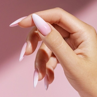 Mão feminina com unhas em formato stiletto e verniz rosa claro em fundo rosa