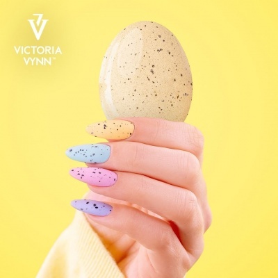 Mão com unhas coloridas segurando ovo manchado sobre fundo amarelo