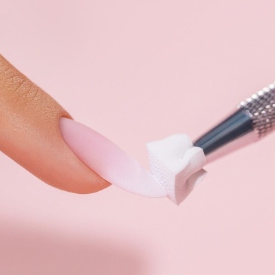 Unha artificial rosa fosca a ser aplicada em unha natural com ferramenta metálica e aplicador de espuma