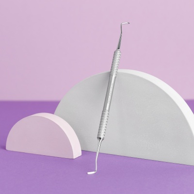 Instrumento odontológico metálico prateado entre formas semicírculos rosa e cinza