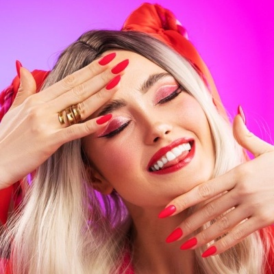 Mulher loira maquiagem rosa, batom e unhas vermelhas com laço vermelho no cabelo