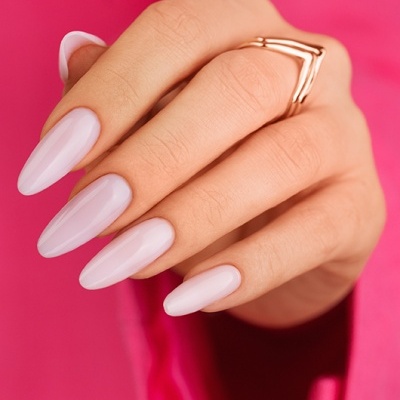 Mão com unhas pintadas de rosa claro e anel dourado em fundo rosa
