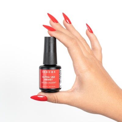 Frasco pequeno de verniz de unhas INOCOS vermelho com mão segurando.