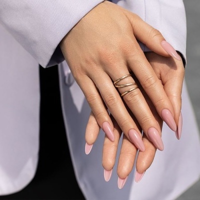Mãos femininas com unhas rosa claro e anel dourado, vestindo casaco lilás