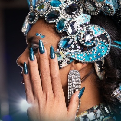 Unhas compridas azul-verde metalizado com coroa decorativa azul e prata e brinco prateado pendente