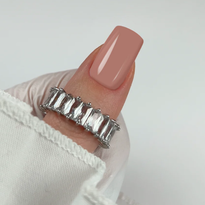 Anel de prata com pedras transparentes retangulares no dedo indicador com unha rosa claro e manga branca.