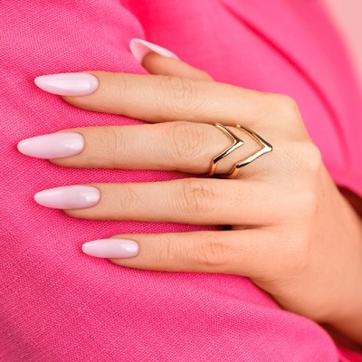 Mão feminina com anel dourado e unhas rosa claro sobre tecido rosa