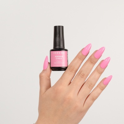 Mão com unhas pintadas de verniz rosa segurando frasco de verniz de gel INOCOS.