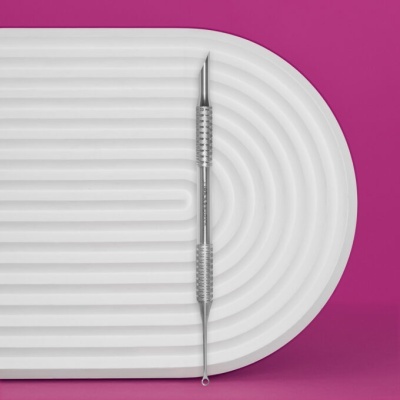 Ferramenta metálica de duas pontas sobre superfície branca com sulcos e fundo rosa