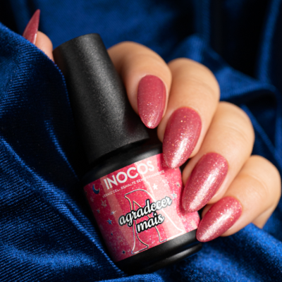 Frasco de verniz INOCOS rosa e unhas pintadas na mão sobre tecido azul