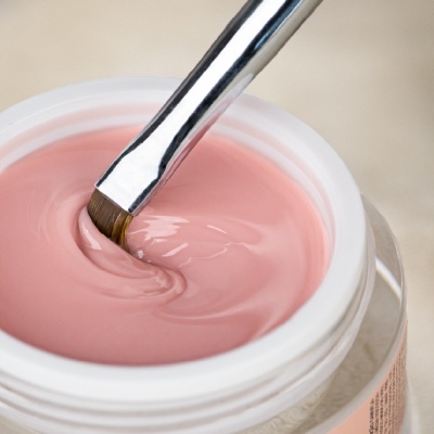 Pote branco com gel creme rosa claro e pincel metálico em fundo neutro