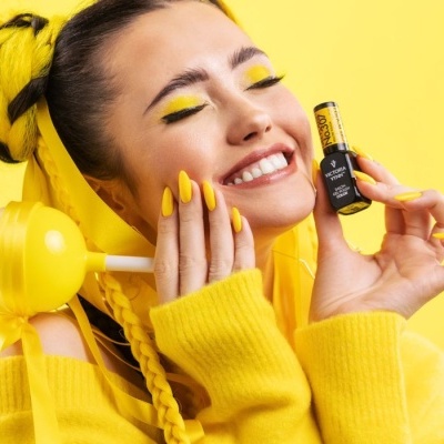 Mulher sorrindo com maquilhagem amarela segurando frasco de verniz de unhas Victoria Vynn