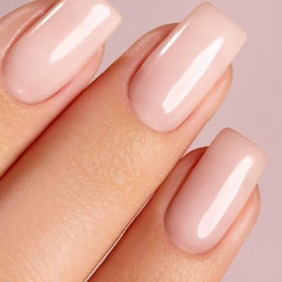 Unhas com esmalte nude brilhante em fundo rosa claro