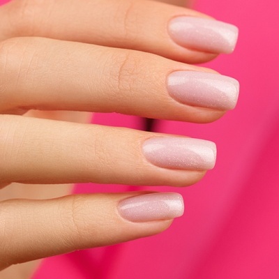 Unhas femininas esmaltadas de rosa claro brilhante frente a fundo rosa