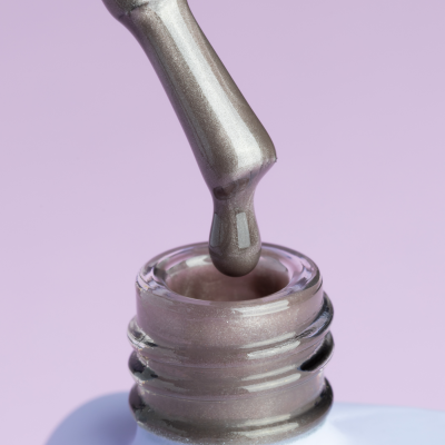 Frasco aberto de verniz de unha prateado com pincel e fundo lilás