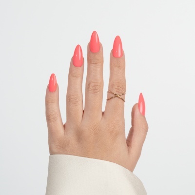 Mão feminina com unhas coral e anel dourado cruzado