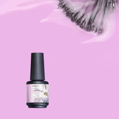 Frasco de verniz para unhas INOCOS cor violeta sobre fundo rosa com flor lilás