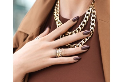 Mão feminina com anéis e colares dourados sobre roupa castanha