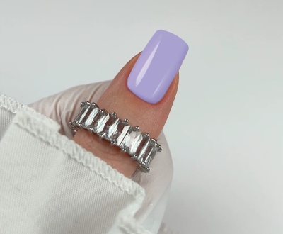 Anel prateado com pedras transparentes em dedo com unha lilás e camisola branca.