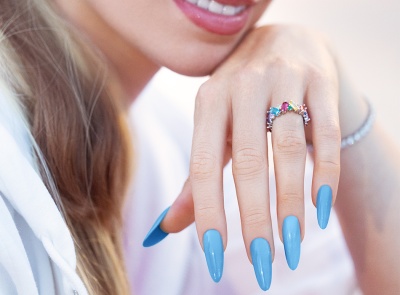 Anel com pedras coloridas em dedo de mão com unhas azuis longas