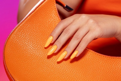 Mala de mão laranja com uma mão com unhas postiças laranja encima
