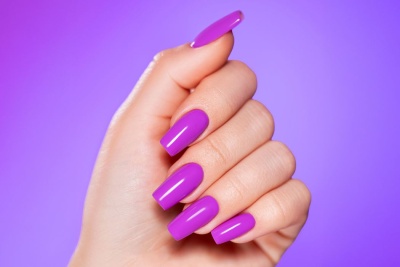 Mão com unhas roxas brilhantes em fundo roxo