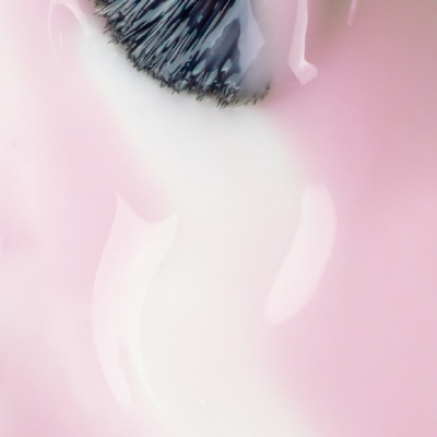 Pincel de maquilhagem com cerdas pretas e líquido branco em fundo rosa