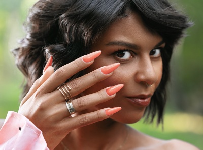Mão feminina com unhas artificiais laranja e anéis, fundo natural desfocado