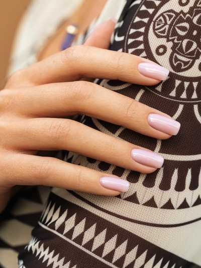 Mão feminina com unhas rosa claro sobre tecido preto e branco com padrão geométrico