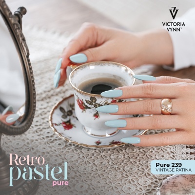 Mãos com unhas azul pastel segurando chávena de chá floral sobre toalha renda