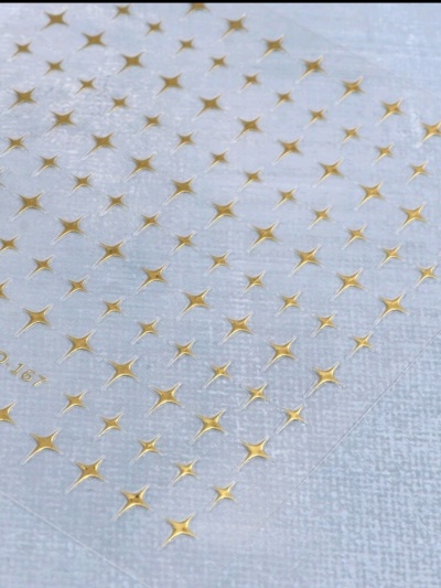 Padrão de estrelas douradas em relevo sobre superfície transparente com texto '10 167'