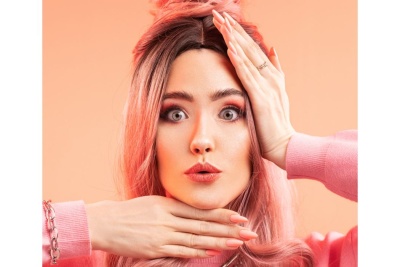 Mulher com cabelo rosa e maquiagem, camisola rosa, fundo laranja