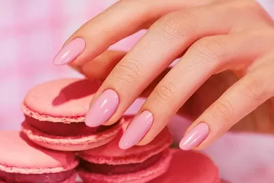 Mão com unhas rosa a tocar em macarons cor de rosa.