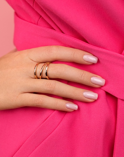 Mão feminina com três anéis dourados simples e unhas rosa claro.
