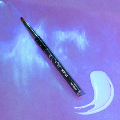 Pincel de precisão preto com pasta branca numa superfície roxa