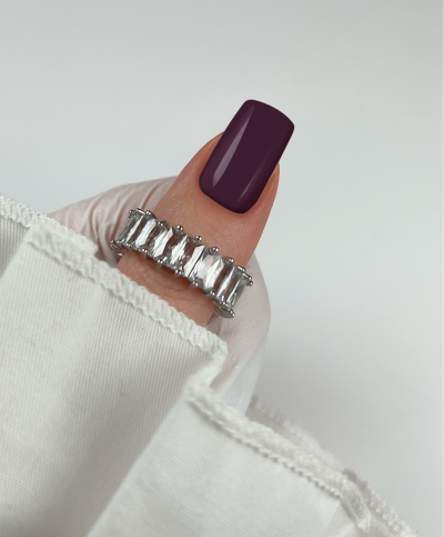 Anel prateado com pedras retangulares em mão com unha roxo escuro e roupa branca