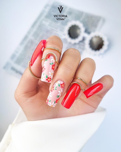 Unhas em gel vermelhas e florais com anéis dourados e fundo desfocado
