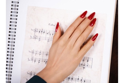 Mão com unhas vermelhas brilhantes sobre caderno com partituras escritas à mão.