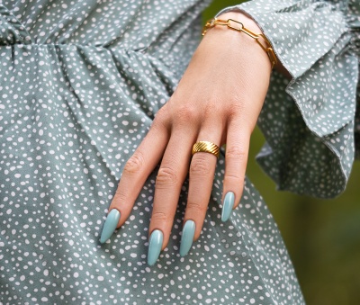 Mão feminina com unhas azul claro e jóias douradas sobre vestido verde com bolinhas brancas