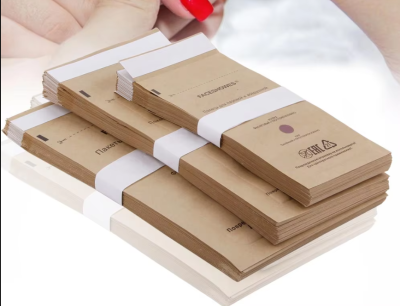 Conjuntos de pads de lixa para unhas em embalagem de papel kraft com faixa branca e mão com unhas vermelhas ao fundo.