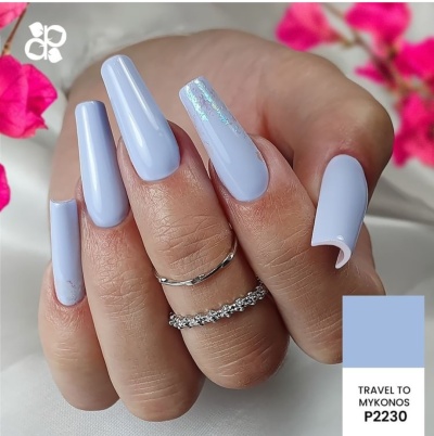 Unhas compridas azuis claras com detalhe holográfico e anéis prateados em mãos femininas